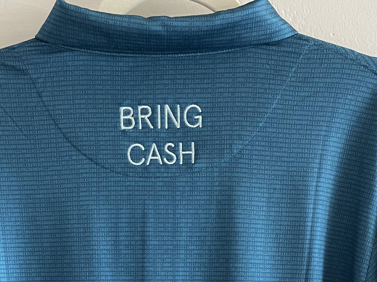 Close-up of the BRING CASH embroidery on the back of the teal Duck Hook Golf polo